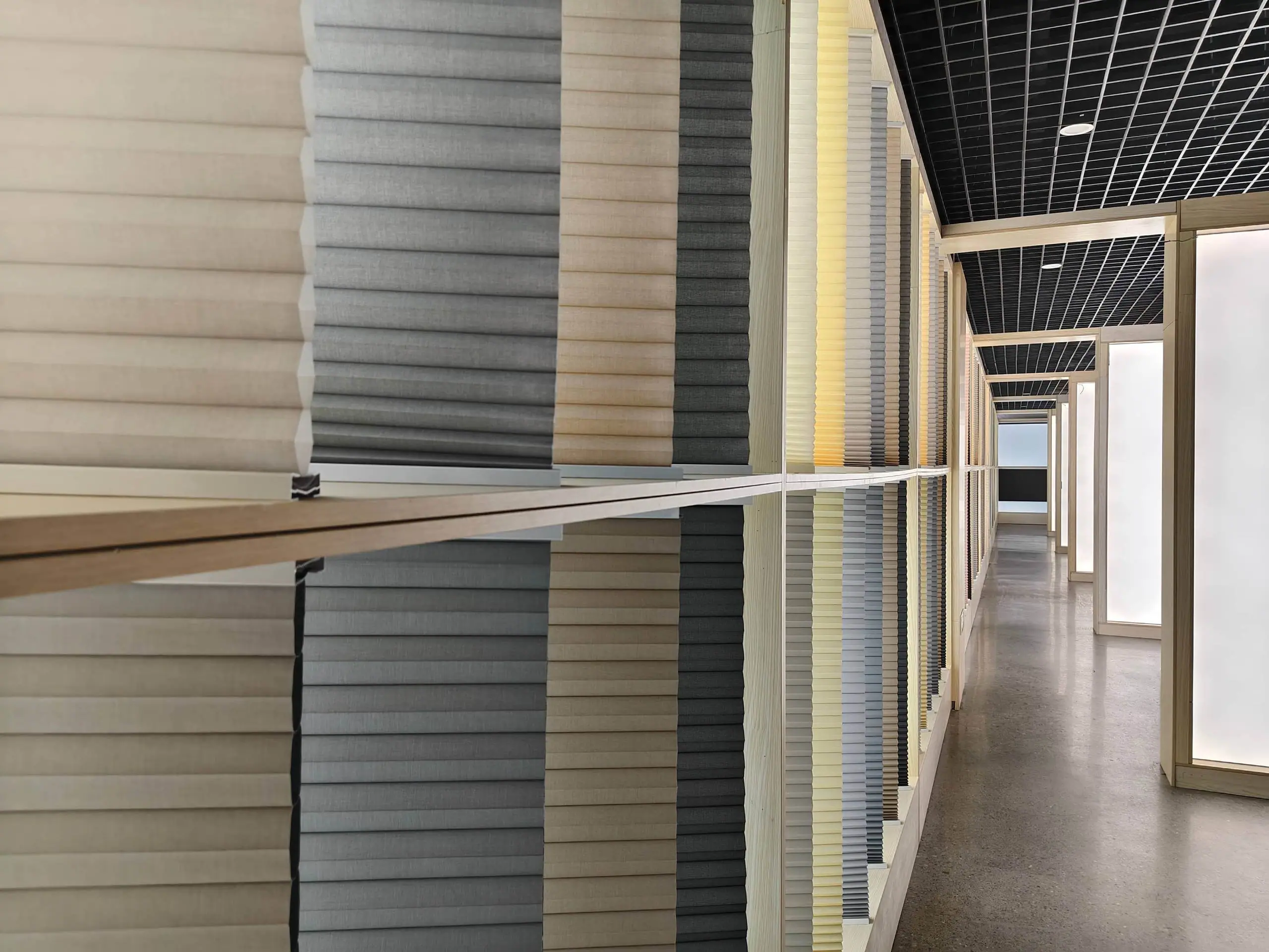 A wall of CAIC honeycomb shades in neutral and grey tones lining the showroom corridor in Shaoxing